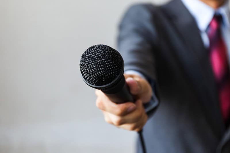 Man in Suit Holding Out Microphone